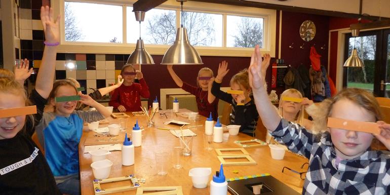 De Kinderen houden hun handenomhoog en zwaaien en houden met de andere hand een tegelstrookje voor hun ogen